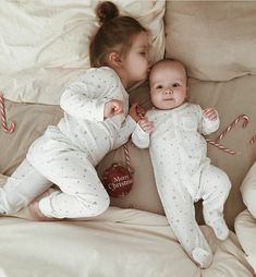 two babies laying next to each other on top of a bed with candy canes