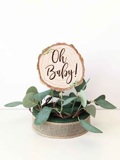 a wooden sign that says oh baby on it next to some leaves and greenery