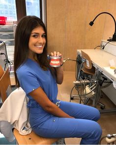 a woman in blue scrubs is sitting on a chair and holding a can of toothpaste