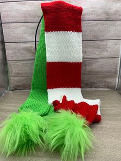 a green and red knitted christmas stocking next to a pair of furry boots