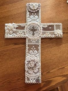 a crocheted cross with flowers on it sitting on top of a wooden table