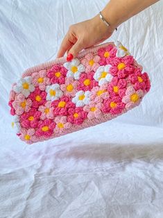 a hand holding a pink crocheted purse with white and yellow flowers on it