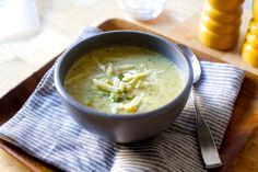 a bowl of broccoli and pasta soup on a wooden tray with silverware