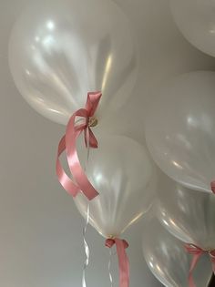 several white balloons with pink ribbons hanging from them