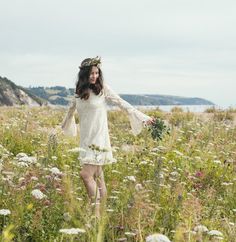 a woman is walking through a field with wildflowers in her hair and wearing a flower crown