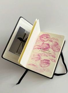 an open book with pink lips on it and a black ribbon around the cover is sitting on a white surface