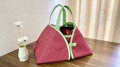 a pink purse sitting on top of a wooden table next to a vase with flowers