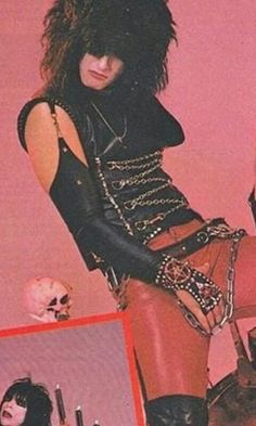 a woman with black hair and leather clothes sitting on a chair in front of a pink wall