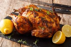 a roasted chicken with lemons and parsley on a cutting board next to a knife