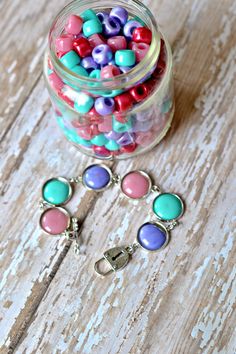 a jar filled with lots of colorful beads next to a pair of scissors on top of a wooden table