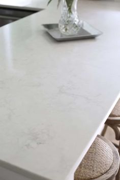 a white counter top in a kitchen next to two chairs and a vase with flowers