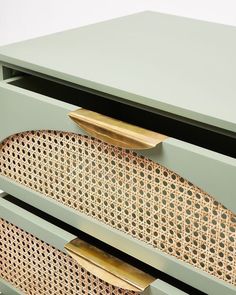 a green dresser with gold handles and wicker drawer pulls on the drawers, in front of a white wall