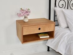 a nightstand with a book on it next to a bed and flowers in a vase