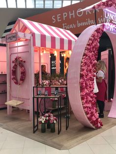 a woman standing in front of a booth with pink flowers on the walls and floor