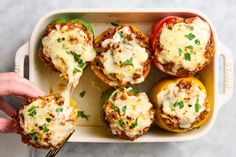 a person is holding a fork over some stuffed peppers in a casserole dish