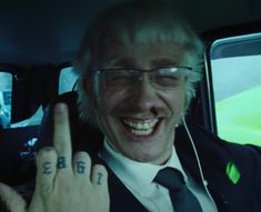 a man in a suit and tie making the peace sign with his hand while sitting in a car