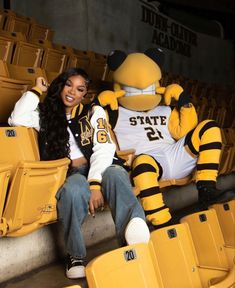 a woman sitting in the bleachers next to a big yellow bird wearing a jersey