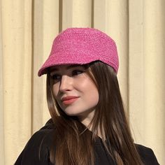 a woman wearing a pink hat standing in front of a curtain with her long brown hair