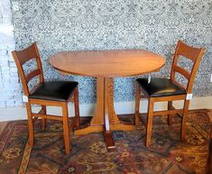 two wooden chairs sitting at a round table in front of a wallpapered wall