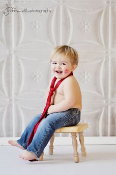 a little boy sitting on top of a wooden chair wearing a red tie and smiling