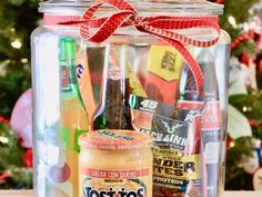 a glass jar filled with lots of different types of food and drinks next to a christmas tree