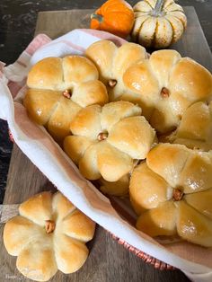 bread rolls sitting in a basket on top of a wooden table next to mini pumpkins