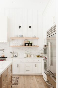 a kitchen with white cabinets and marble counter tops, along with open shelving above the stove