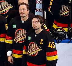 three men in black hockey jerseys standing next to each other