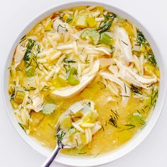 a white bowl filled with chicken noodle soup and garnished with fresh herbs