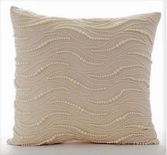 a white pillow with beading on the front and back side, sitting on a white surface