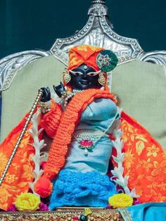 a doll is sitting on a chair with an orange shawl and headdress