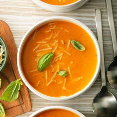 two bowls of tomato soup with cheese on top and basil leaves in the bowl next to it