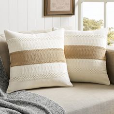 two pillows sitting on top of a couch in front of a framed picture and window