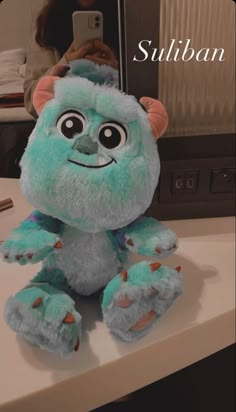 a blue stuffed animal sitting on top of a counter next to a cell phone with the caption sullban