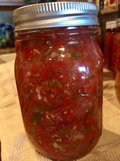 a jar filled with lots of red liquid on top of a wooden table next to other jars