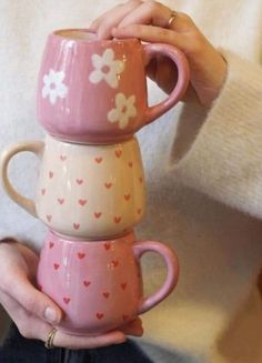 a woman holding three cups in her hands with hearts and flowers painted on the mugs