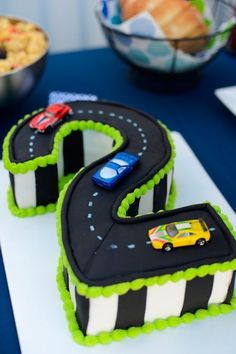 two birthday cakes with cars on them sitting on a table next to a bowl of food