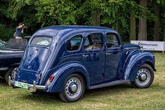 an old blue car is parked on the grass near another one in front of some trees