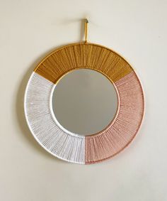 a circular mirror hanging on the wall with gold and white trimmings, along with a hook