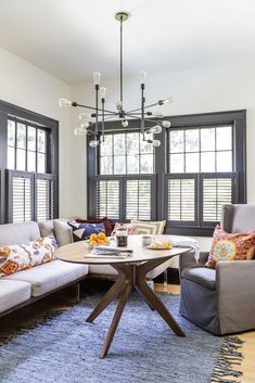 a living room with couches, chairs and a table in front of two windows