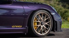 the front end of a purple sports car with gold rims and yellow brake pads