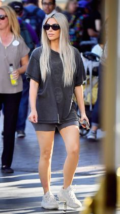 a woman with long blonde hair is walking down the street in shorts and sneakers while wearing sunglasses