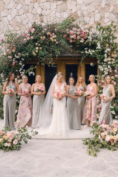 a group of bridesmaids standing in front of a stone building with flowers and greenery