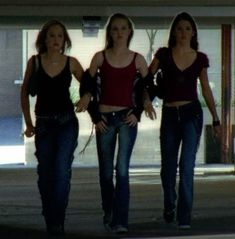 three girls walking down the street in jeans and red tops with their hands on their hipss