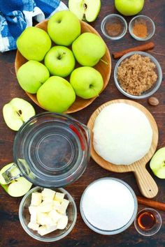 apples, sugar and other ingredients are on a wooden table with bowls filled with them