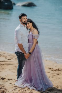 a man and woman standing next to each other on top of a sandy beach with the ocean in the background