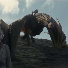 a man standing next to a giant dinosaur on top of a hill