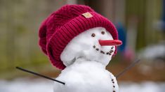 a snowman wearing a red hat and holding a pair of knitting needles in its mouth