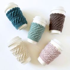 four knitted coffee cups sitting next to each other on top of a white table