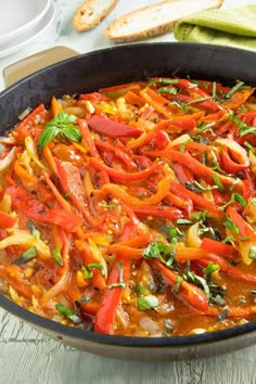 a skillet filled with peppers and onions on top of a wooden table next to bread